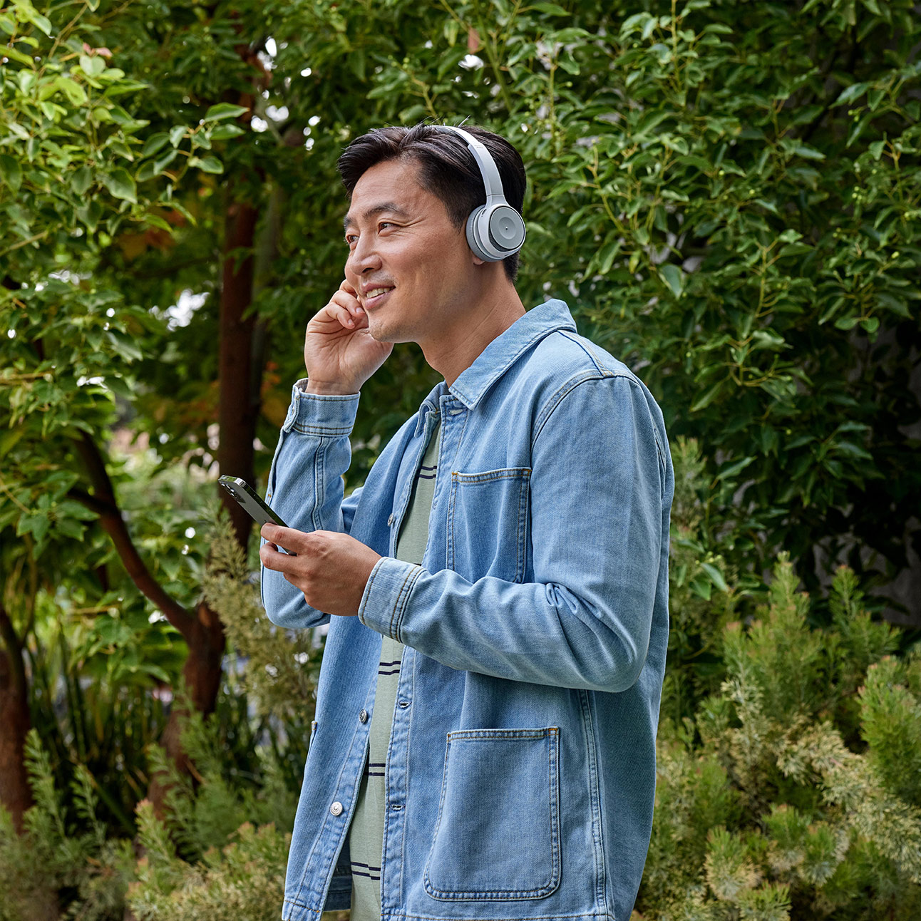 Person walking outdoors interacts with a headset while on a mobile call.