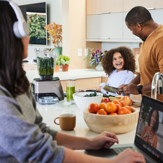 Family in kitchen with one family member having a video call on a laptop