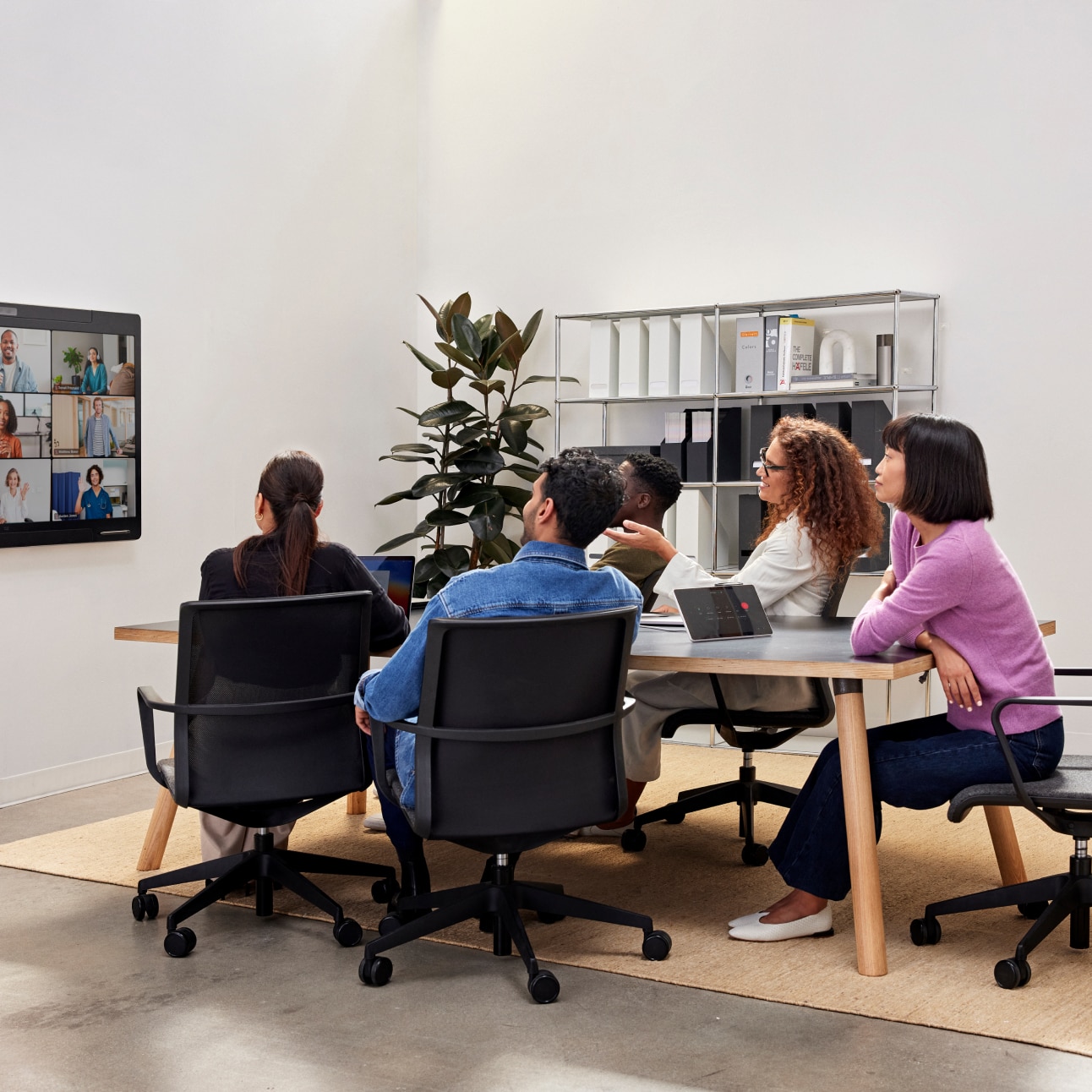 A group of colleagues in a conference room collaborates with several other colleagues via a video meeting.