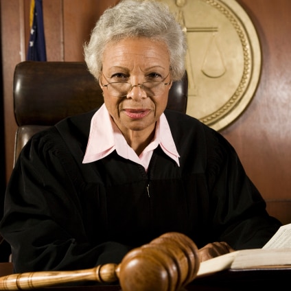 A judge sits at the bench, with a gavel in the foreground.