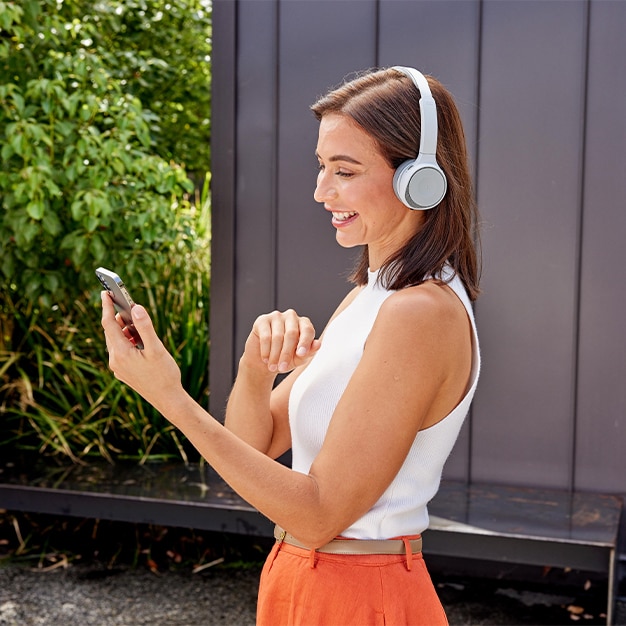 A woman walking outside while in a meeting on her mobile device wearing a Cisco 730 Headset.