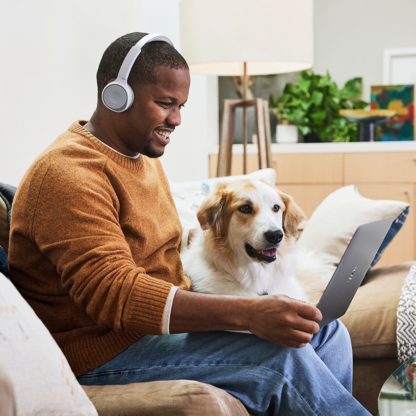 Man working from home with an open laptop and Cisco 730 Headset while sitting on a couch with his dog.