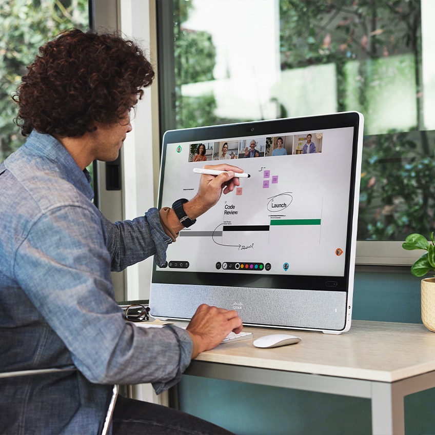 Person, die während einer Videokonferenz auf dem Cisco Desk Pro an einem digitalen Whiteboard arbeitet – mit einem Eingabestift in der Hand sowie Tastatur und Maus auf dem Schreibtisch.