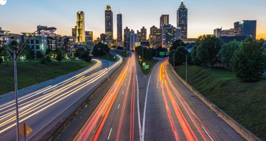 The highway at dusk. The city skyline and lights can be seen in the background.