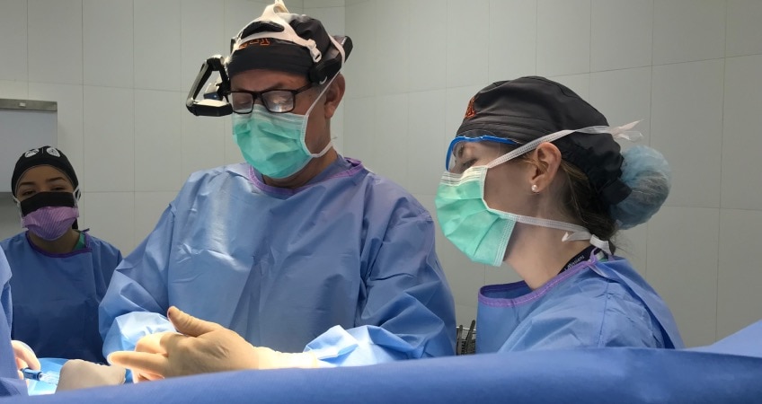 Surgeon in RealWear headset stands with 3 other medical professionals, leveraging Webex Expert on Demand during a surgery.