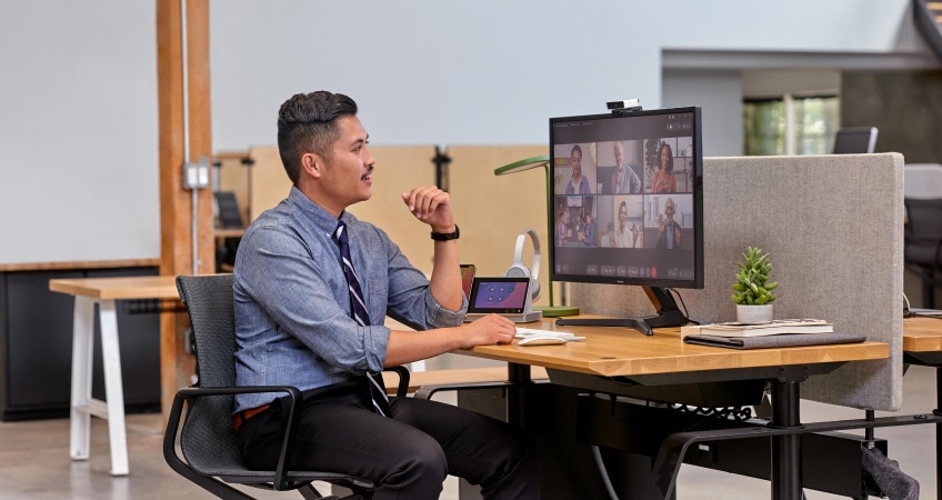 Person sits on his deck in the office, chatting with several colleagues via a video meeting.
