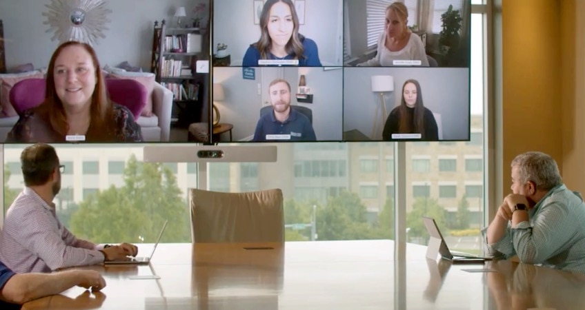 Colleagues in a conference room collaborate with several other colleagues via a video meeting.