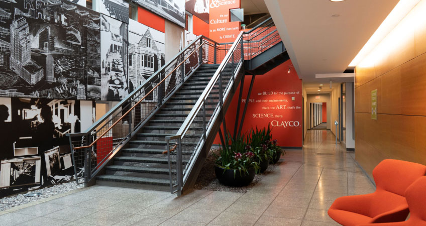 A photograph of the Clayco offices, showing a staircase, the Clayco logo, and a bright red chair.