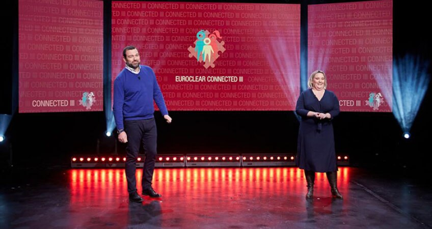 Two speakers stand on a stage, in front of a red backdrop with the words Euroclear Connected III