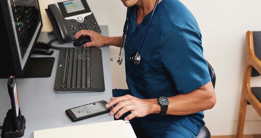 A medical professional seated at a desk glances at content on a mobile phone.