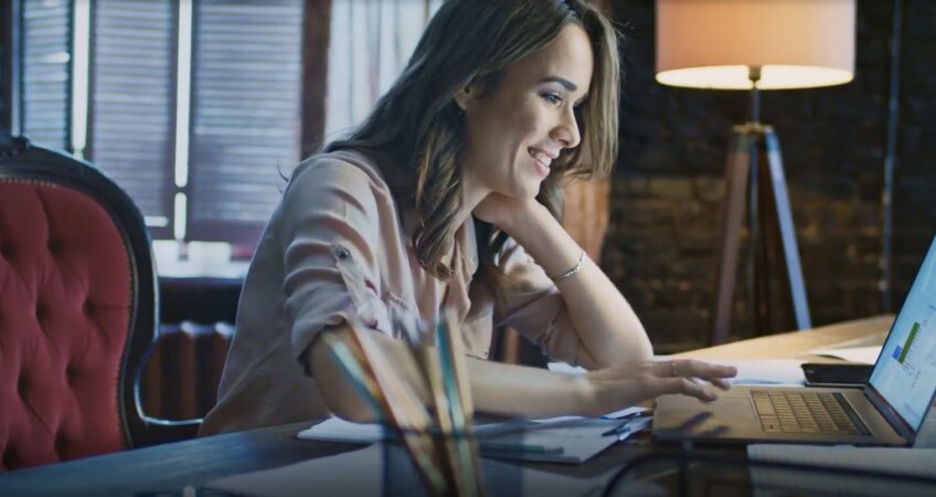 A smiling professional works remotely on a laptop from a home office.