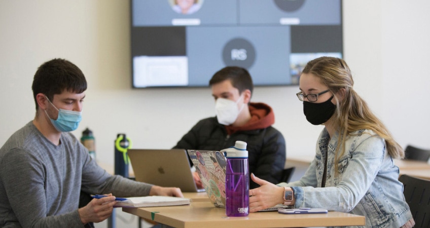 Three masked students learn in-person while others video conference in via Webex during a hybrid course at UW-Whitewater.