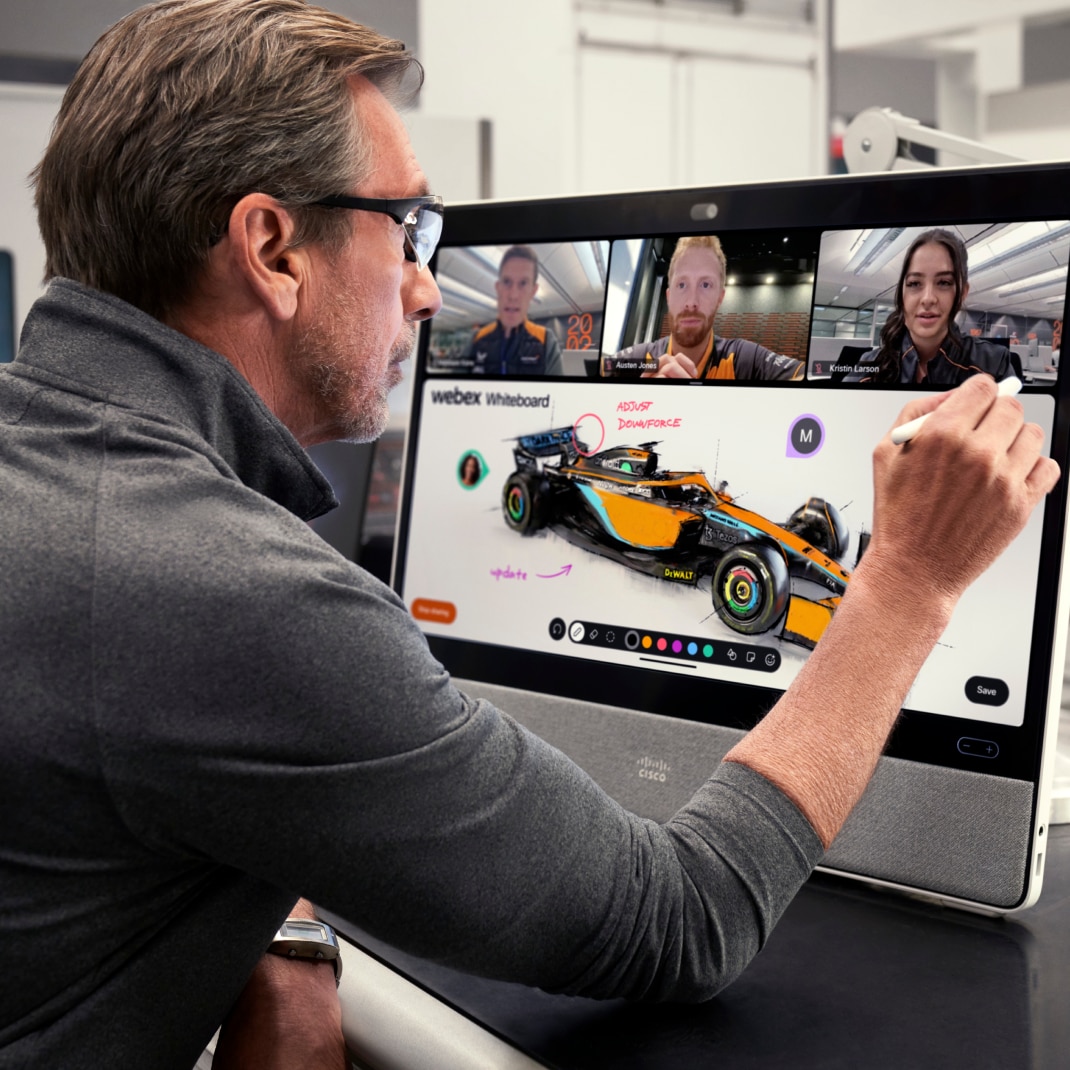 A team member at a desk uses a digital whiteboard to work on a car design while video conferencing with 3 others.