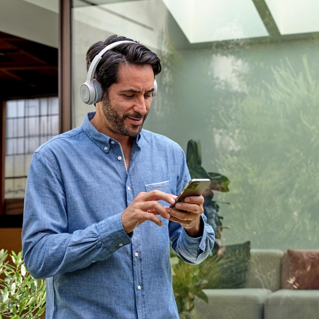A professional in a headset stands outside a building, collaborating via Webex on a mobile phone.