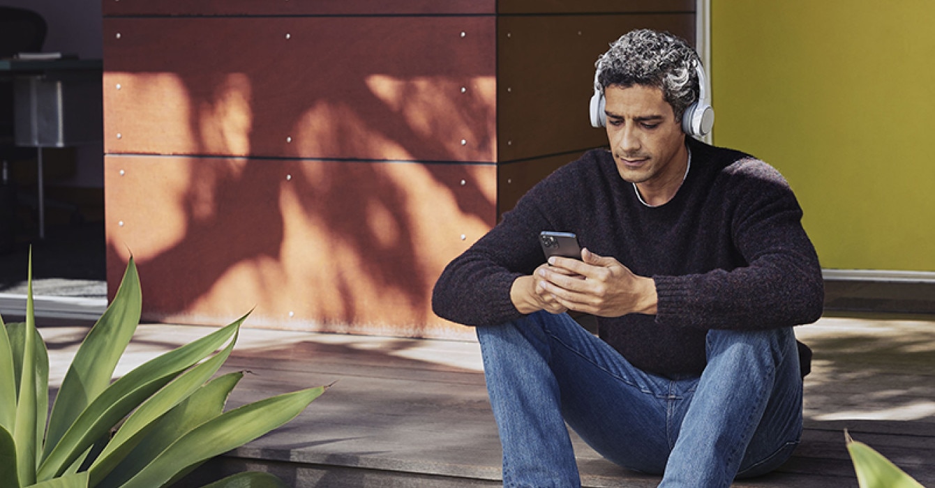 A person sits outdoors and uses a mobile device with a headset.