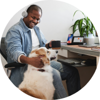 relaxed person (playing with dog) with headphones on, seemingly connected to Webex docking device on desk