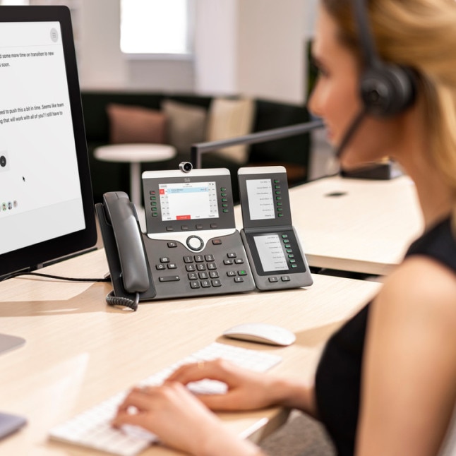 person at desk working on desktop pc while their VOIP device in prominent in the background