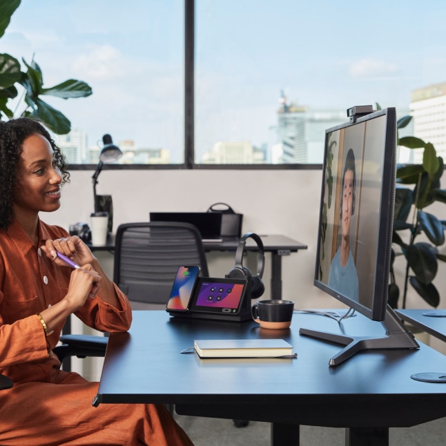 person in office having a video call on monitor, while Webex dock/desktop device is featured in background