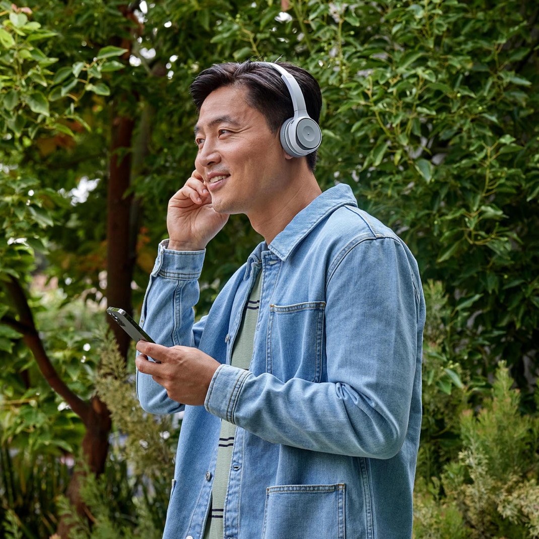 A person adjusts a pair of headphones while holding a mobile device.