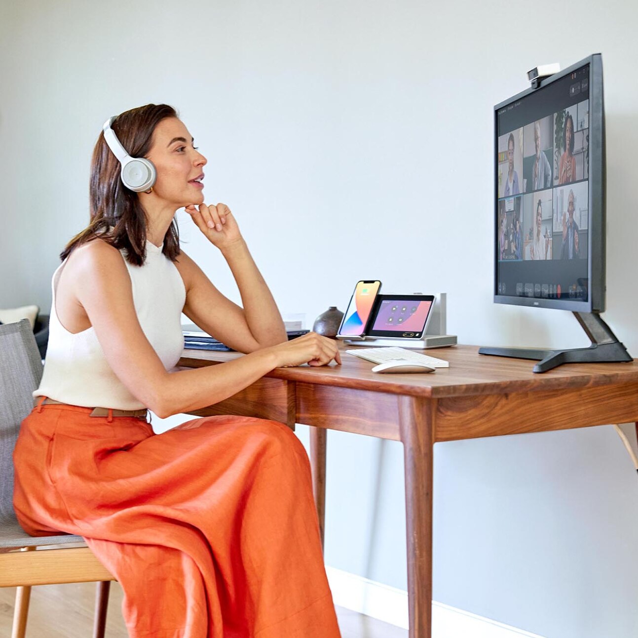 A person wearing headphones sits at a desk, watching a meeting on a computer monitor. A Webex Desk Hub sits on the corner of the desk.