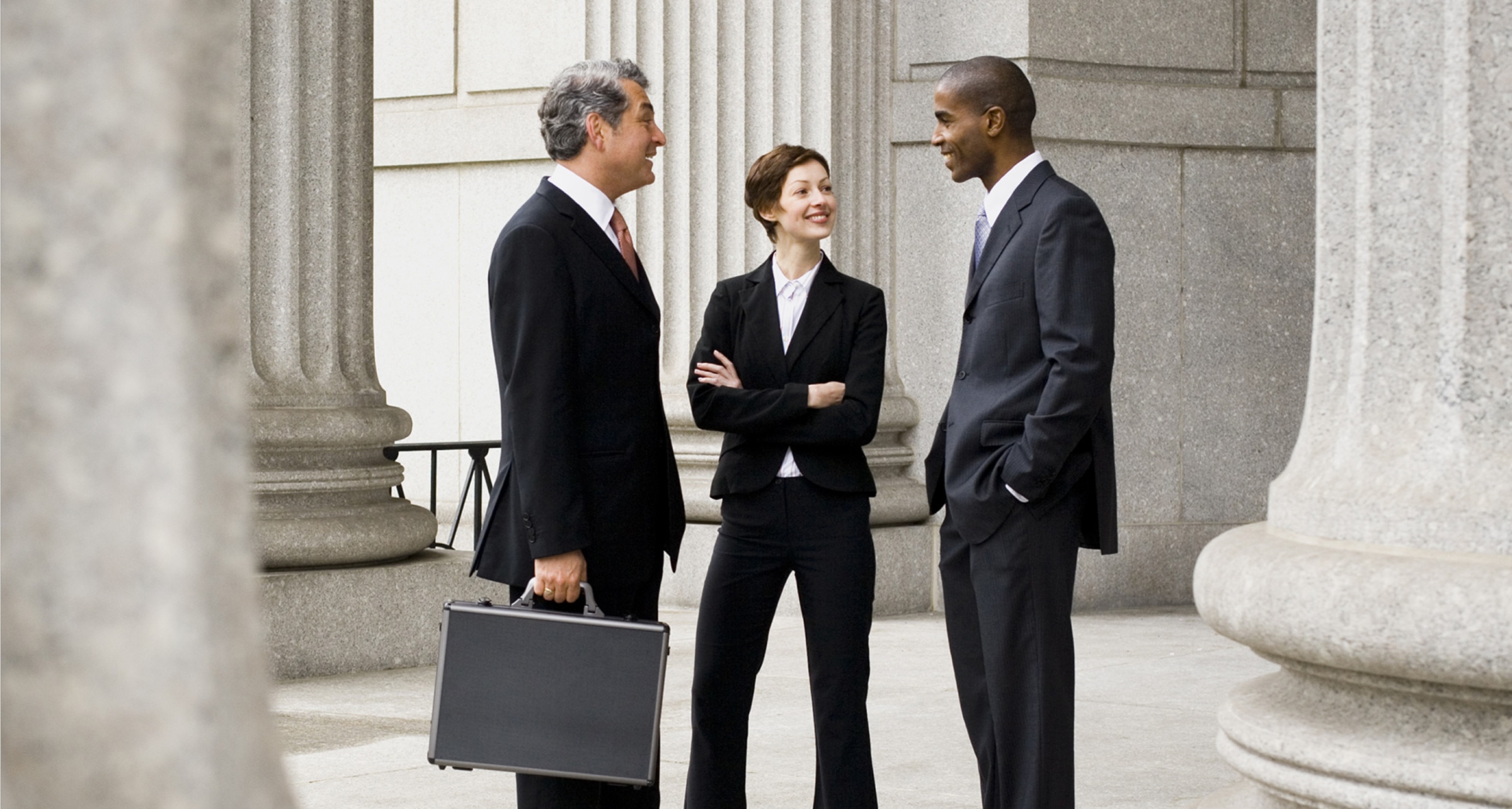 Three people have a friendly chat outside a government building