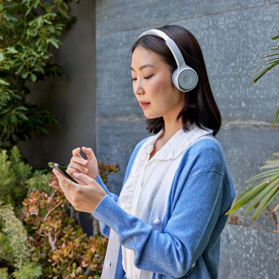 A person wearing headphones looks down at a mobile device.