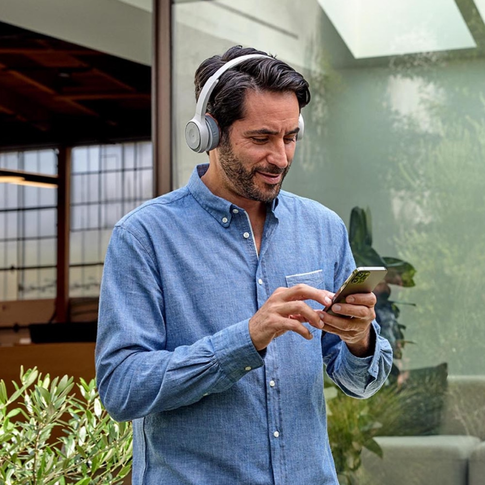 A person wearing headphones smiles while looking at a mobile device.