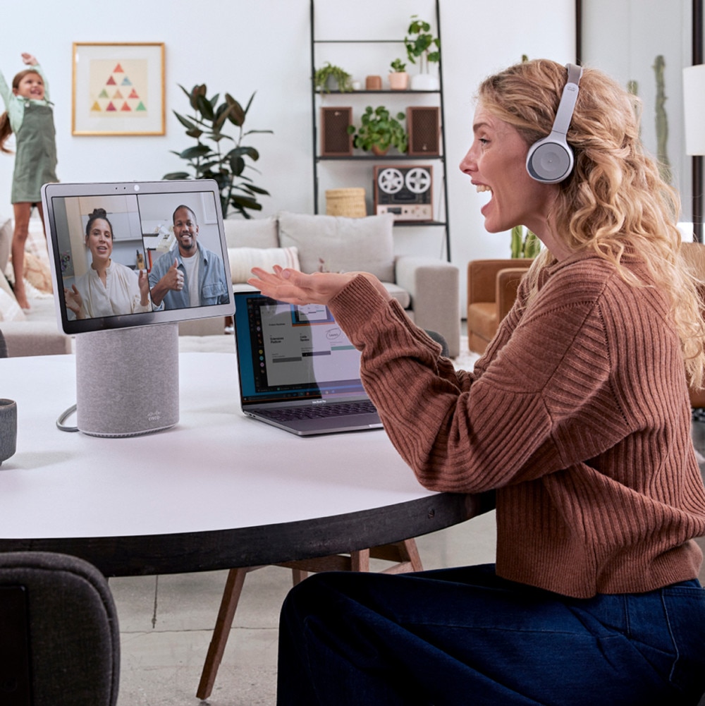 A person uses a Webex Desk Mini to have a conference call as child plays in the background.