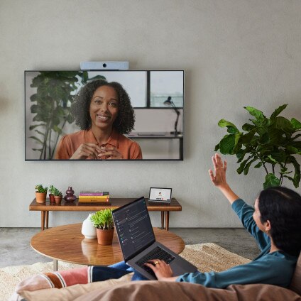 Person working from home waves to another person video conferencing in, displayed on the large screen on the wall.