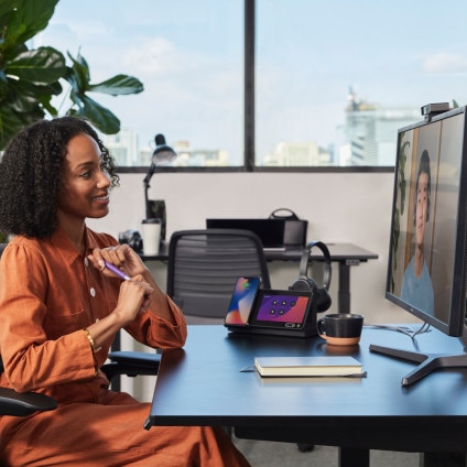 Smiling person in an office sits at her desk, video conferencing with a colleague.