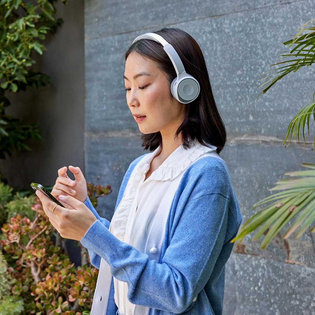 A person wearing headphones stands outside, checking a mobile device.