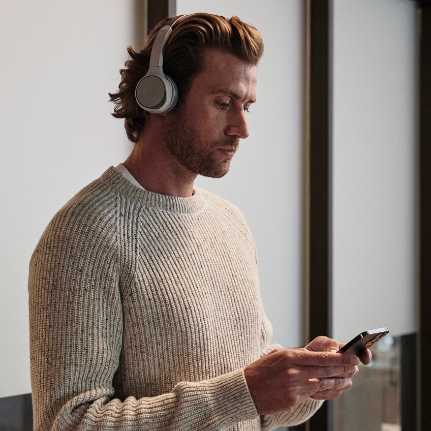 A professional wearing a headset and a sweater listens to a voicemail on his iPhone.