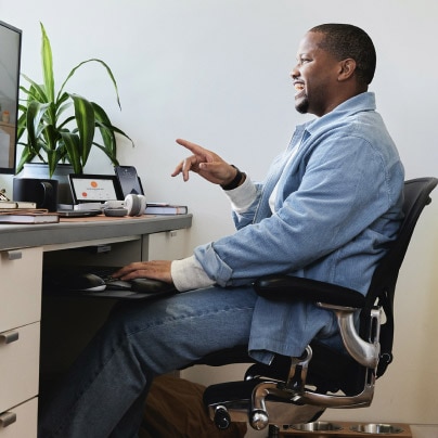 Side view of a person seated at a desk engaged in a video meeting.