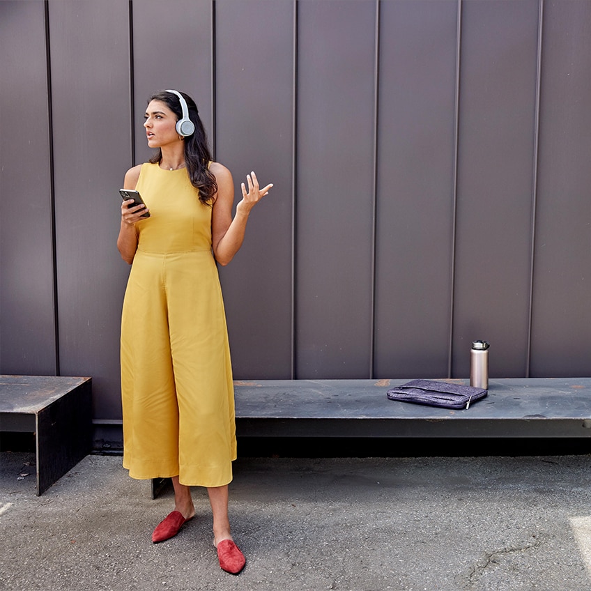 A professional outdoors on a meeting with a mobile device. A laptop and water bottles placed on a bench behind her.