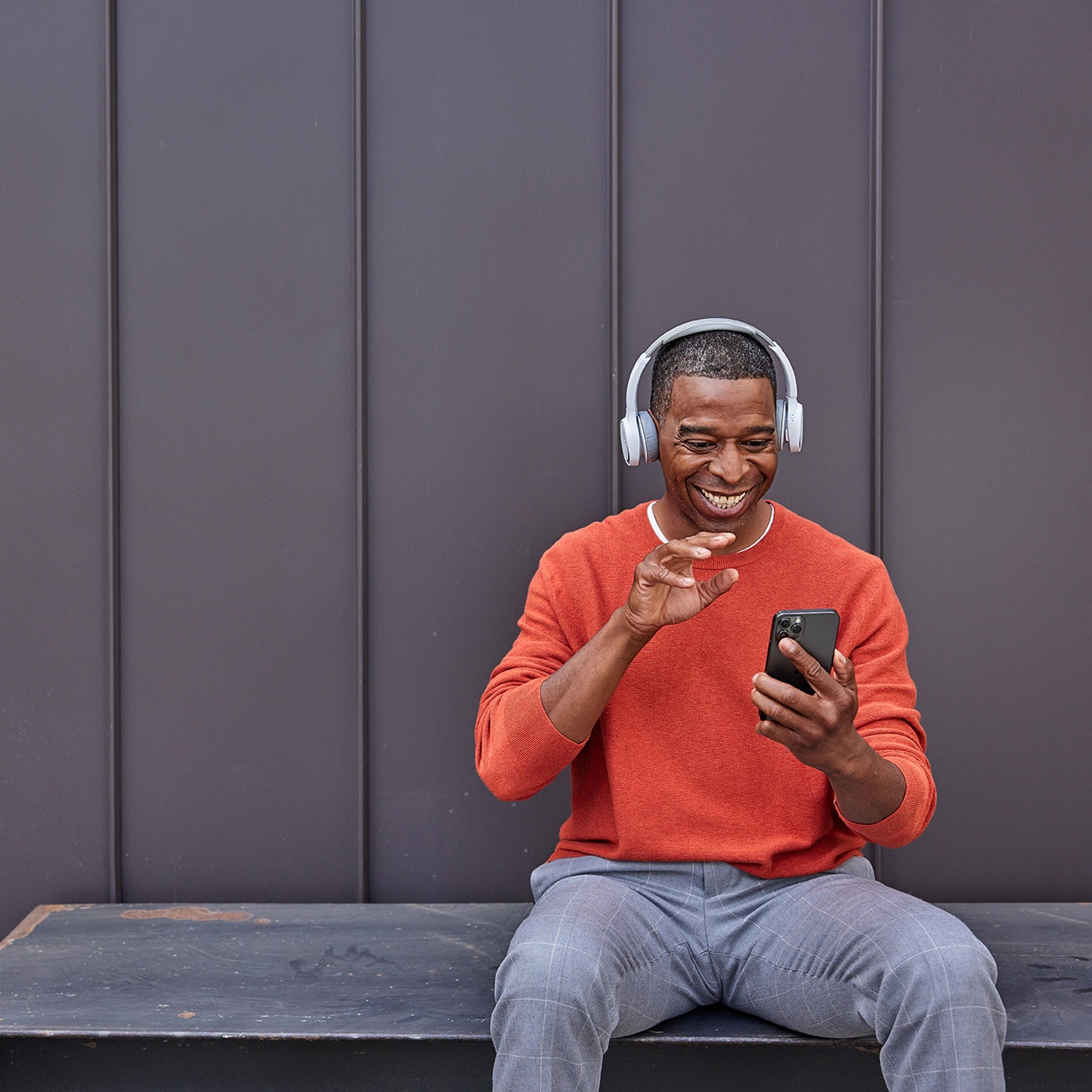 A person sitting on a bench wears a headset  while in a video call on his mobile devices.