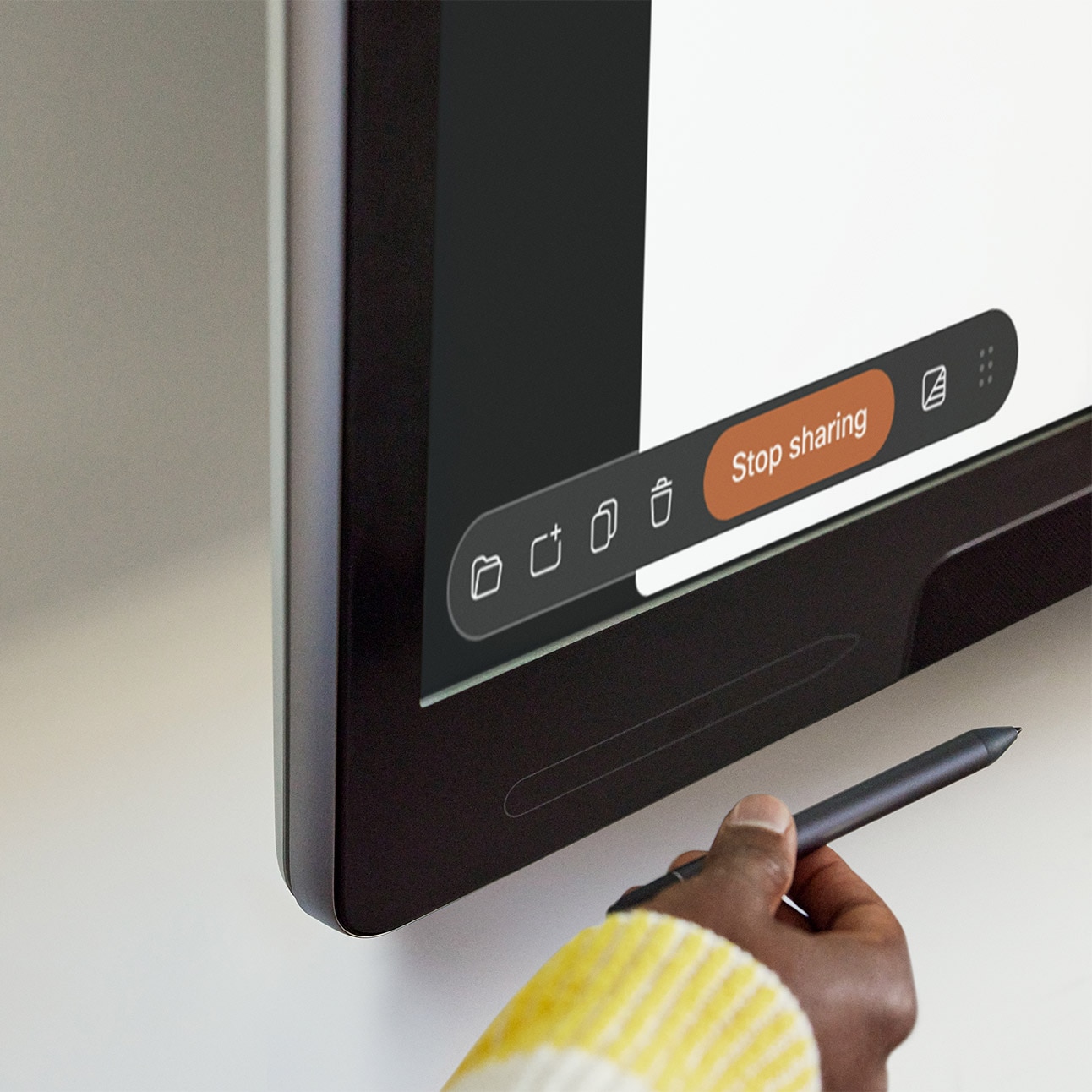 Close up of the bottom left corner of the wall-mounted Cisco Board Pro showing the magnetic board pen holder and the menu bar of the digital whiteboarding user interface. One person's hand is shows as she is about to attach the magnetic board stylus to the Board Pro.