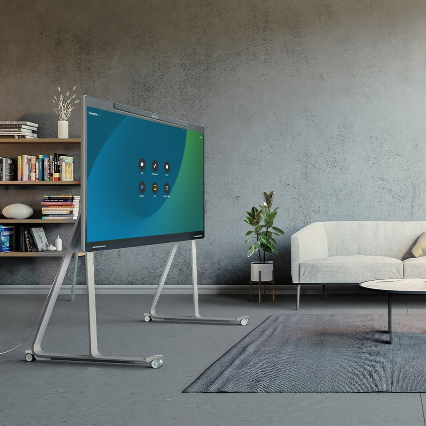 A rendering of an empty open studio featuring the wheel-stand Cisco Board Pro. The touch display of the Board Pro shows the home user interface of the Cisco RoomOS platform with icons to join video meetings, start whiteboarding, share content, and open web applications.