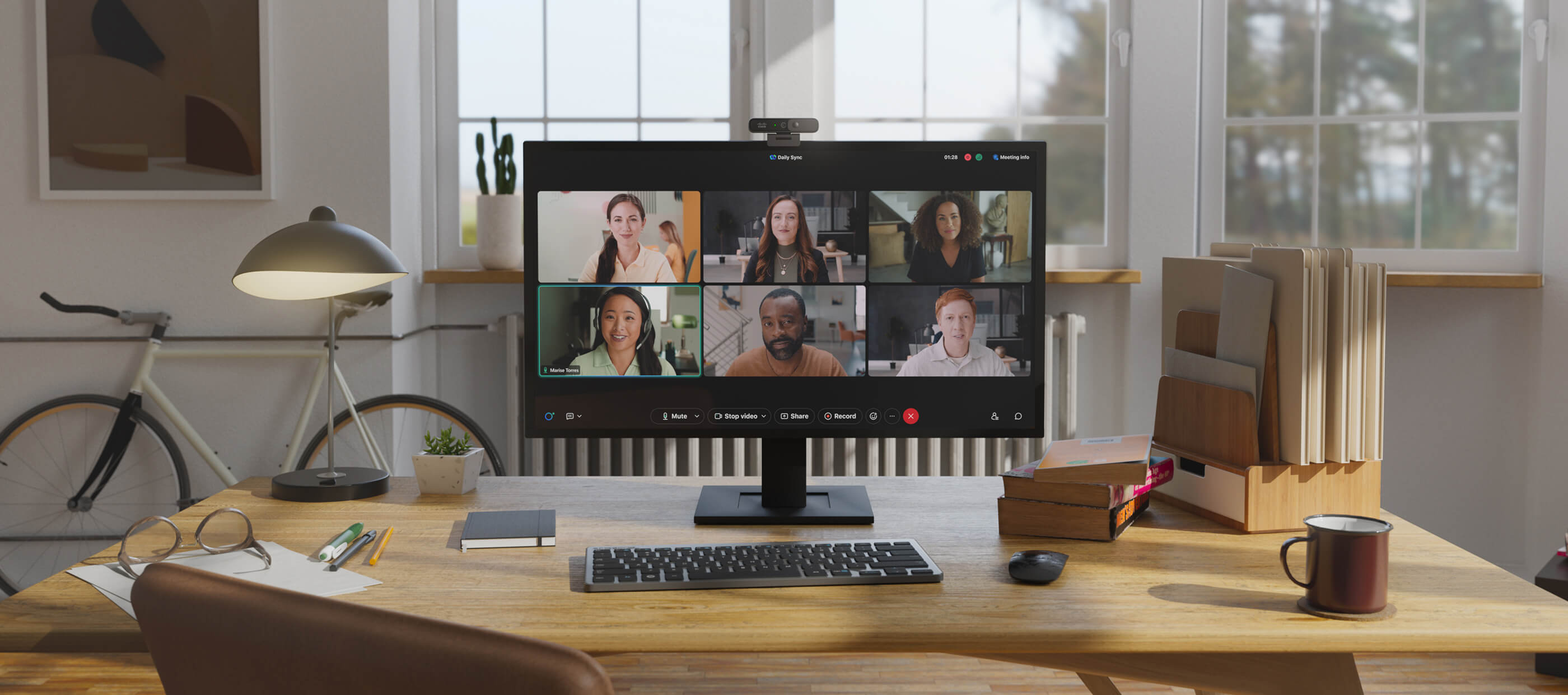 The Desk Camera 1080p on a monitor in a home office. On the monitor screen, six colleagues are having a video meeting.