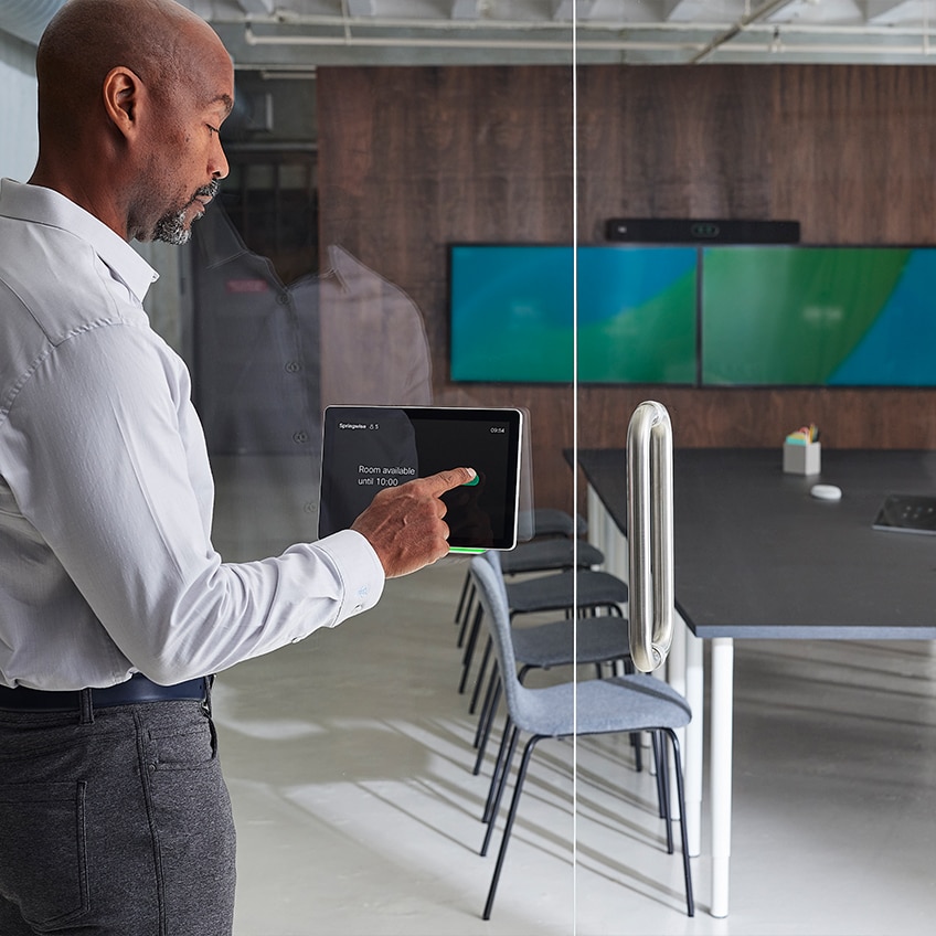 A professional stands outside a meeting room and books the space using the Cisco Room Navigator.