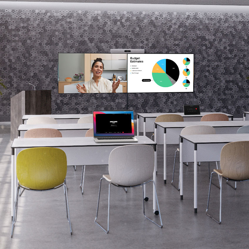 A large empty workspace with a podium at the front of the room. Room Kit EQ is mounted above two displays showing a presentation and remote participant on Webex.