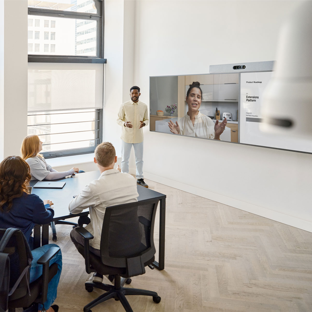 Four people collaborating in meeting room with the Cisco Room Kit EQ mounted on top of two displays.