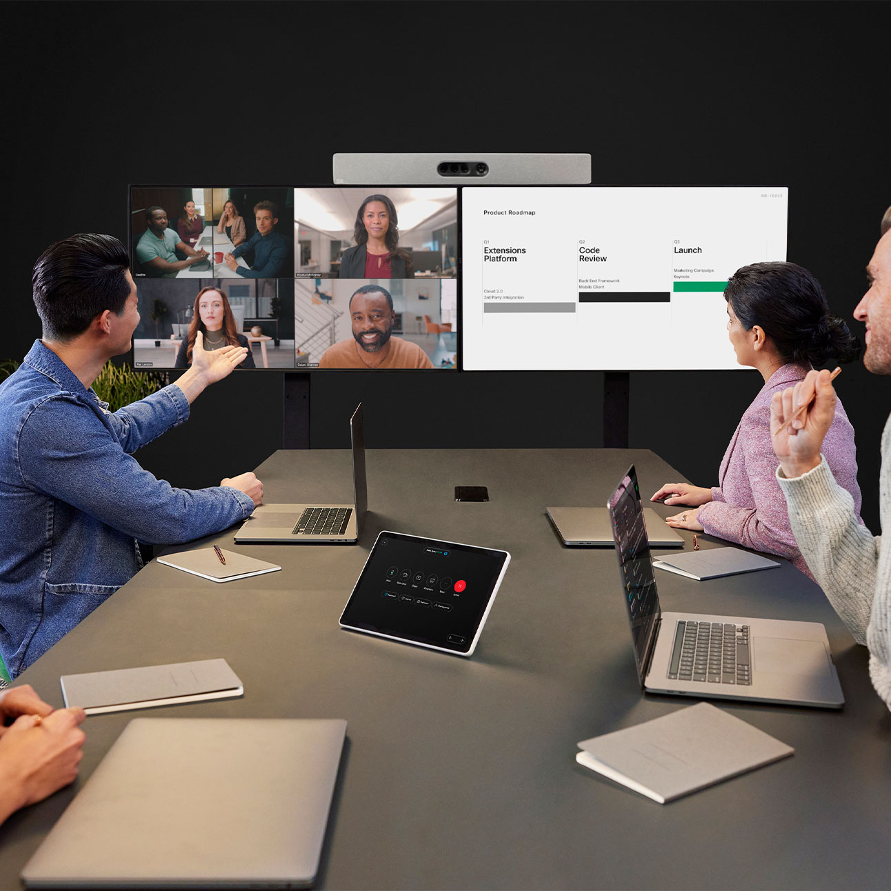 Four people collaborating in a local meeting room. Room Kit EQ mounted on two displays. Room Navigator on the tabletop.