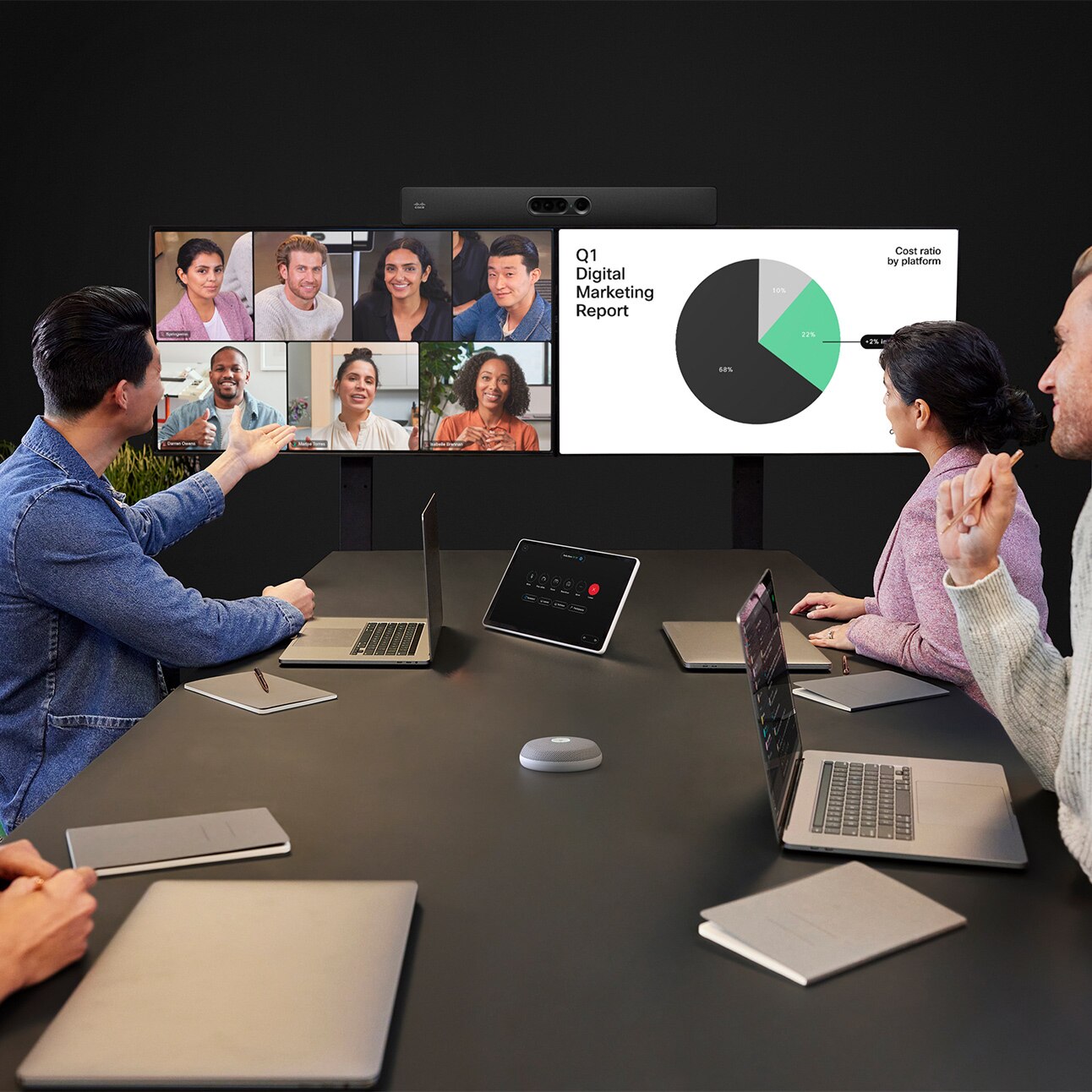 A large meeting room showing the Cisco Quad Camera bar mounted under dual external screens displaying live video and shared content in a video meeting. The Cisco Room Navigator room controller and Cisco Table Microphone Pro devices are located on the conference table.