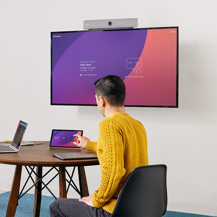 Person in a conference room equipped with a Cisco Room Bar video collaboration bar starts a video meeting using the Cisco Room Navigator touch panel.