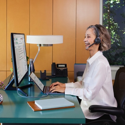 person working at desktop computer, wearing headphones, probably on a call