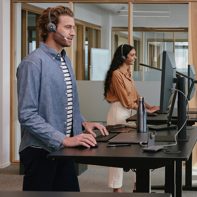 two people at standing desks with headphones on looking busy