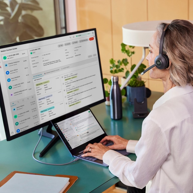 person with headphones typing on laptop (with external monitor) at desk