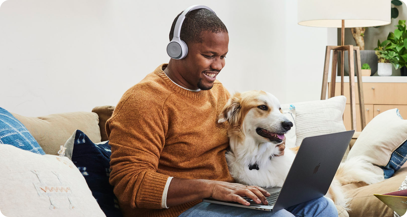 犬と一緒に座り、ヘッドホンを付けて楽しそうにノートパソコンを使う人