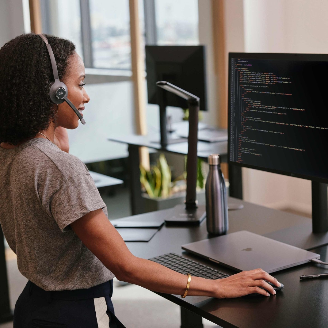 A businessperson with a headset on works at a standing desk.
