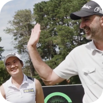 A golfer waves while another golfer smiles nearby.